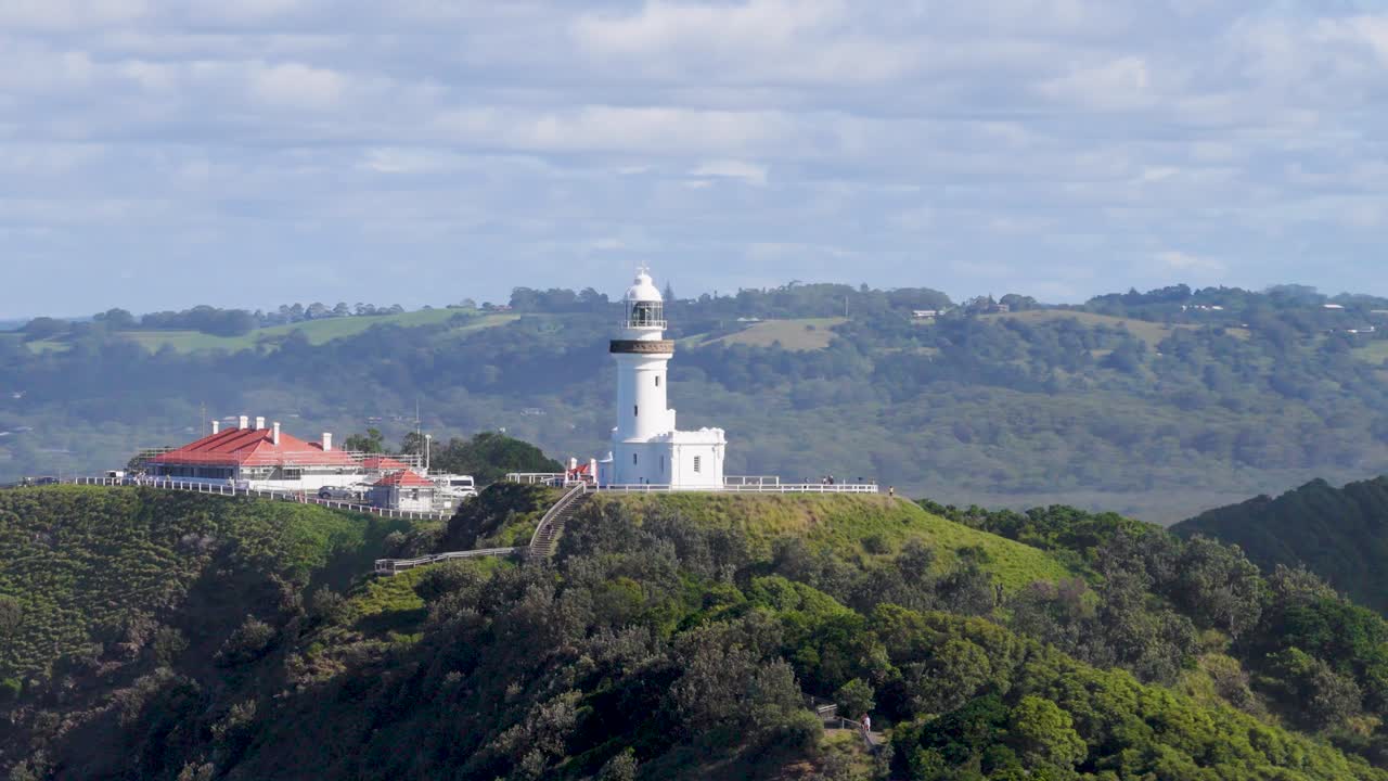 Drone footage captures Byron Bay lighthouse on a sunny day, highlighting coastal landscape and ocean views
