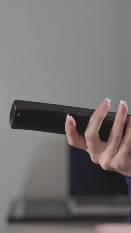 hand of redhead woman holding remote control on blurred background. tired housewife changes channels on tv sitting in living room at home closeup