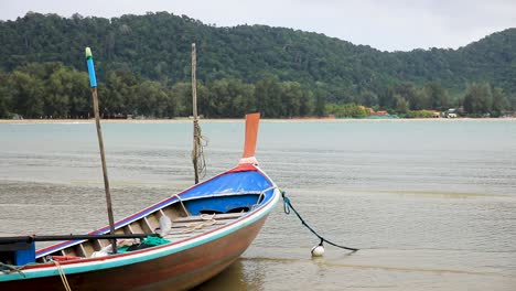 thai longtail boat anchored along the beach by rope on the island of koh lanta in thailand with water and waves