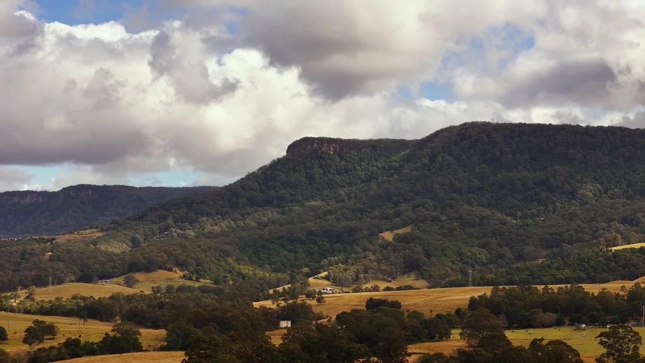 Scarpata di Illawarra che si erge sopra campi ondulati sotto nuvole drammatiche, sfondo aereo di media distanza