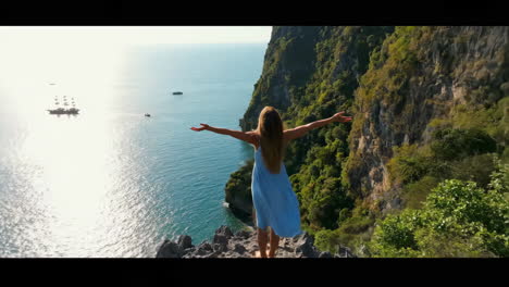woman on cliff overlooking stunning tropical ocean and sailing ships