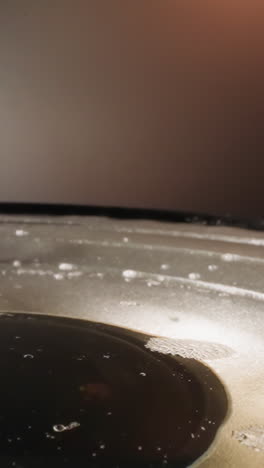 Layer of transparent water with foam on dynamic panel in room against grey wall. Particles of white powder fall on liquid making circles on water macro