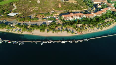 Bird's-eye-view-pan,-sandals-resort-sandy-barbara-beach-and-boat-pier-dock,-aerial-drone