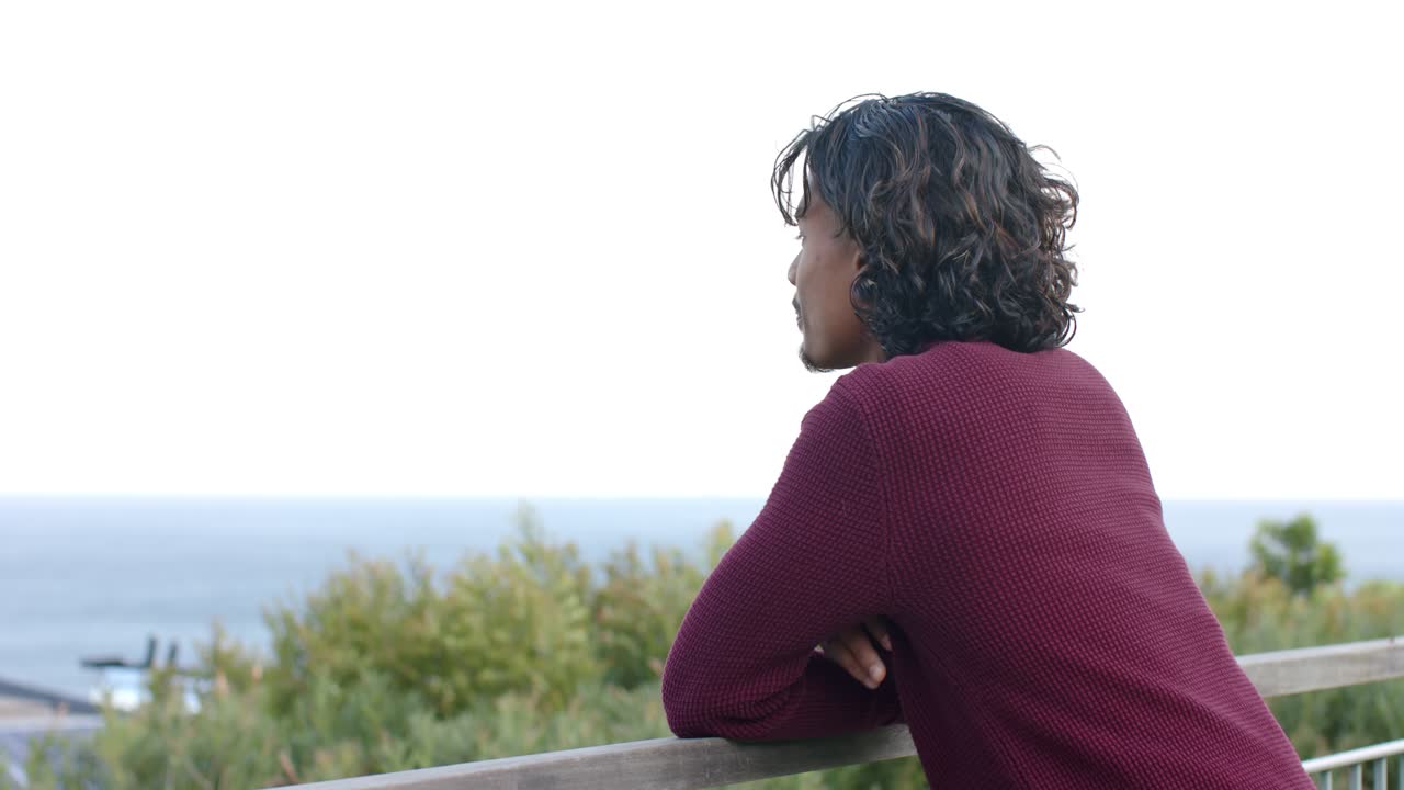 When coastal view appears, man is leaning on railing admiring ocean then smiling at camera