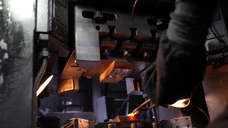 Worker adjusting a forging press machine with a glowing hot metal edge visible