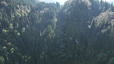 high altitude aerial over kossdalen valley, revealing lush forest and winding hairpin road turns in sunlight