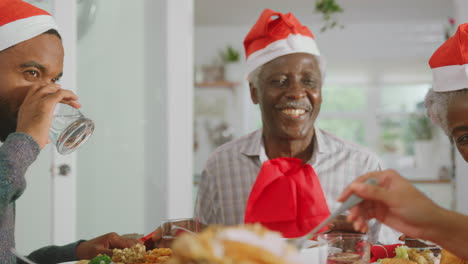 familia de varias generaciones con sombreros de santa disfrutando de la comida de navidad en casa juntos