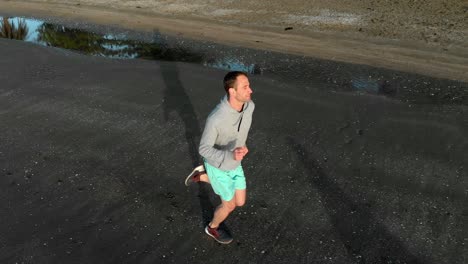 toma aérea de un joven en forma corriendo en una playa en auckland, nueva zelanda