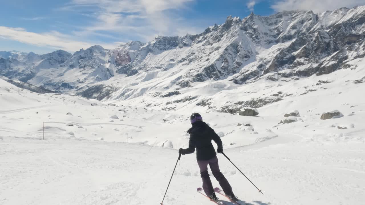 Movimento lento di una sciatrice in curva su una pista in discesa nella stazione sciistica di Cervinia, con vista mozzafiato sulla catena montuosa.