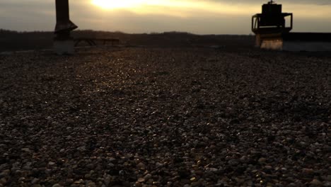 smooth dolly on roof of abandoned industrial building. rocks and pebbles shine in evening light