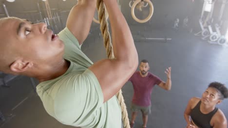 Diverse-group-fitness-class-motivating-man-climbing-rope-at-gym,-in-slow-motion