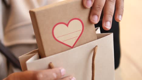 hands placing a heart-decorated gift box into a paper bag
