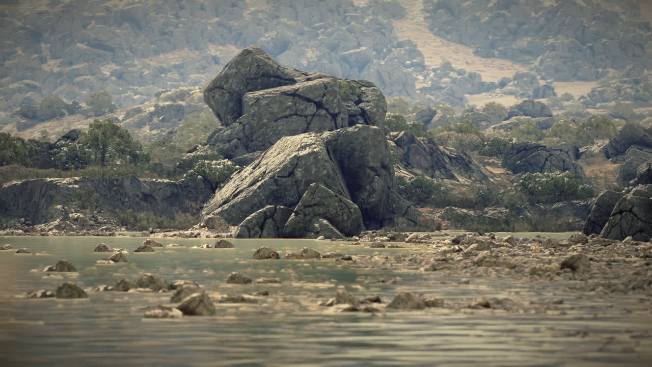 Large rock formation alongside a calm water body in a hilly landscape at noon