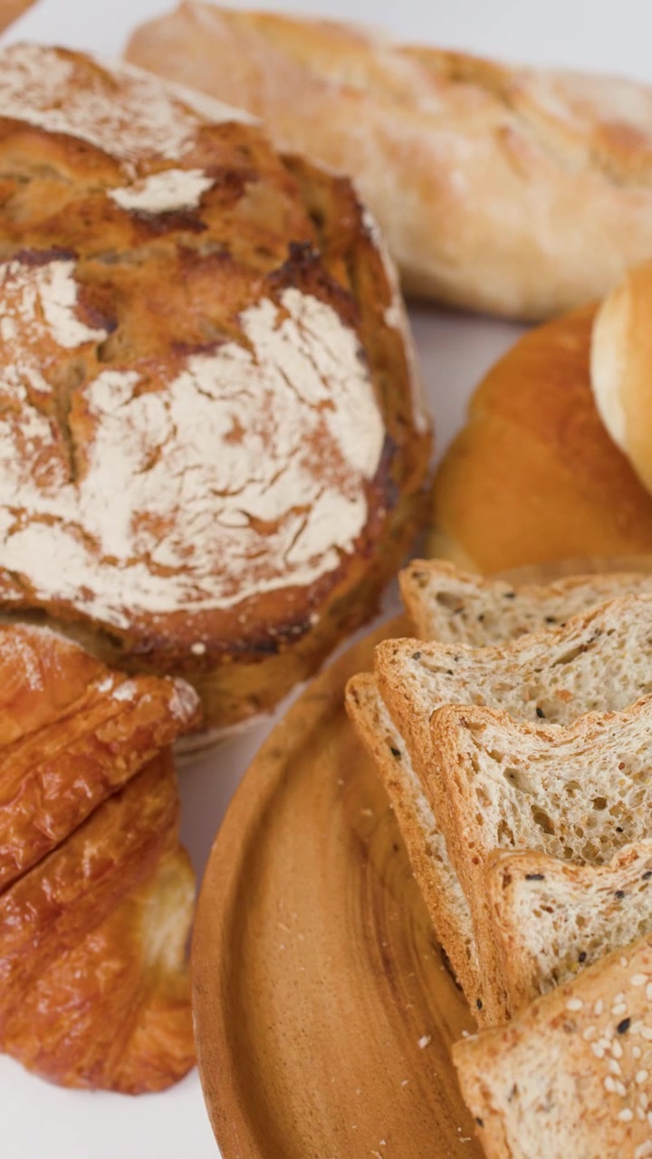 Primo piano panoramico di pane a lievitazione naturale, croissant e pane multicereali a fette su un piatto di legno.