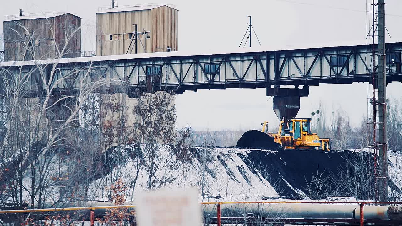 bulldozer sprinkles a pile of coal on the territory of the power plant. Coal covered with snow