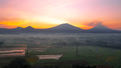 Sunrise-over-mountains-in-the-distance-with-fog-covered-rice-fields-at-morning,-Indonesia