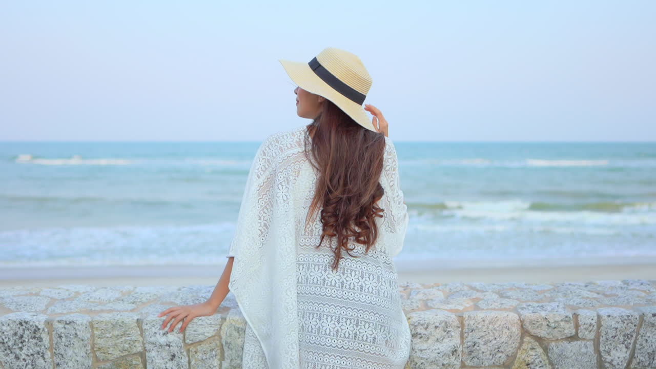 A beautiful woman looking out to the ocean as waves crash onto the white sandy beach