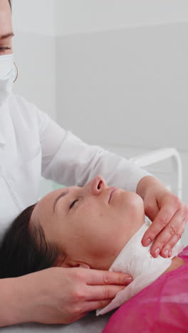 cosmetologist doctor wipes woman face and neck cleaning procedure with paper wipes in beauty clinic