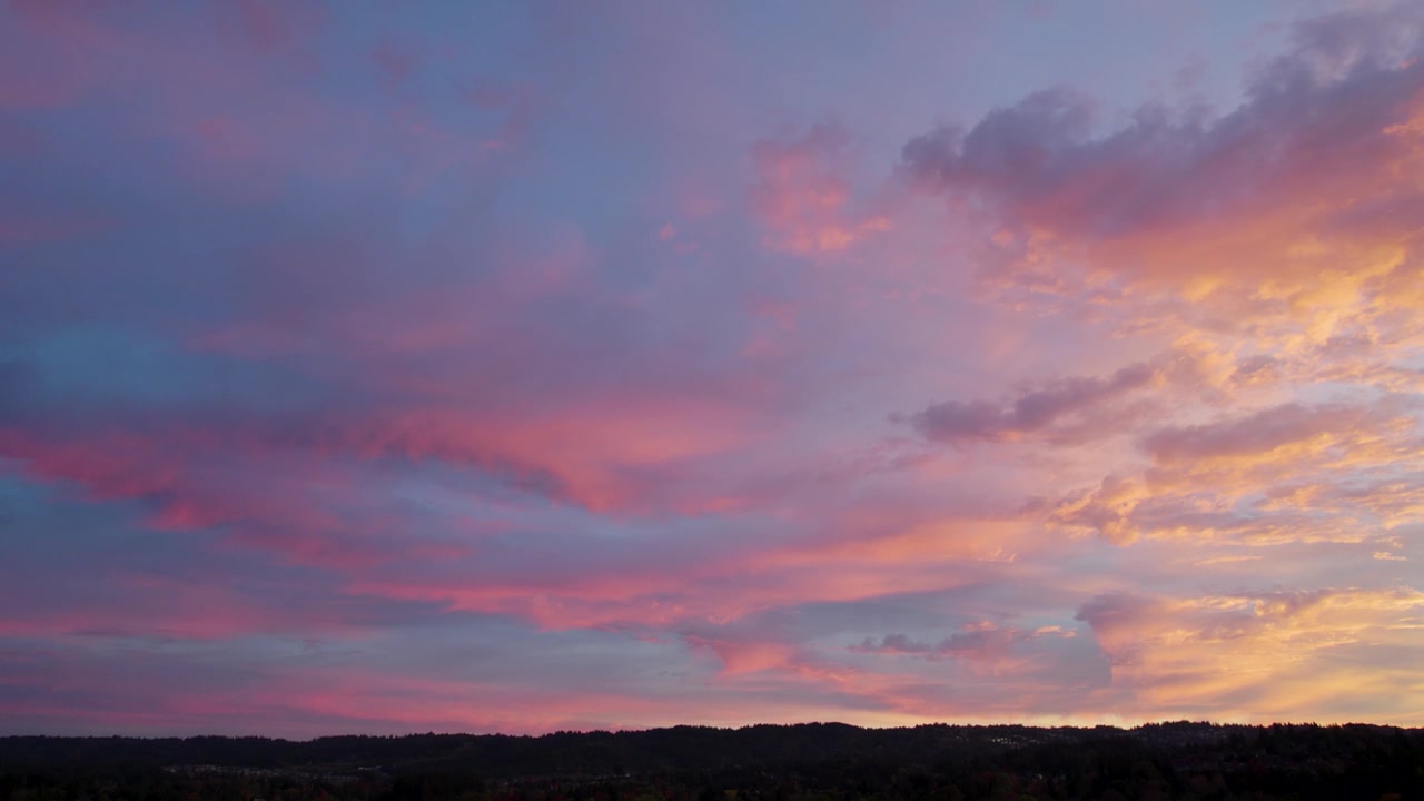 Una dolce alba bagna l'orizzonte in toni rosa e blu. Il drone rivela nuvole luminose che si muovono dolcemente, incorniciando la tranquilla bellezza dell'alba.
