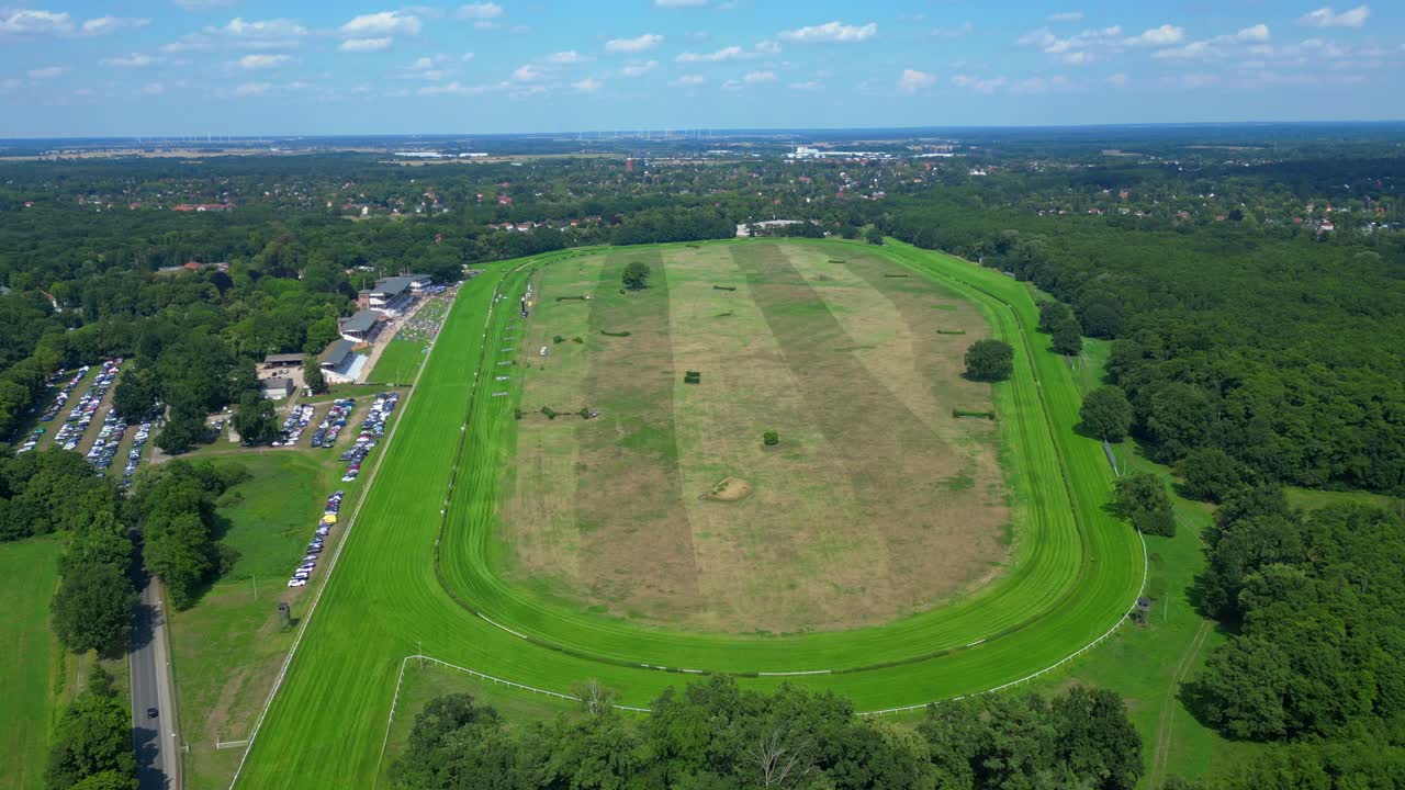 Horse gallop racecourse near a forest in Germany, parking lot visible. Dramatic aerial view flight descending drone