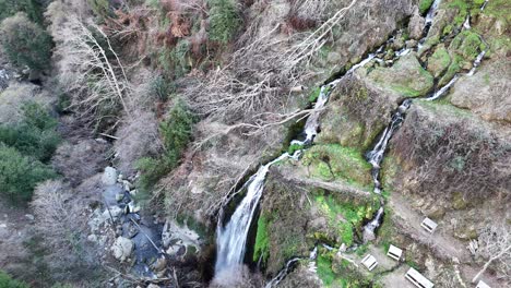 Natürlich-Schöner-Wasserfall,-Der-Vom-Gipfel-Des-Berges-Fließt,-Drohnenansicht-Von-Stühlen-Neben-Dem-Wasserfall