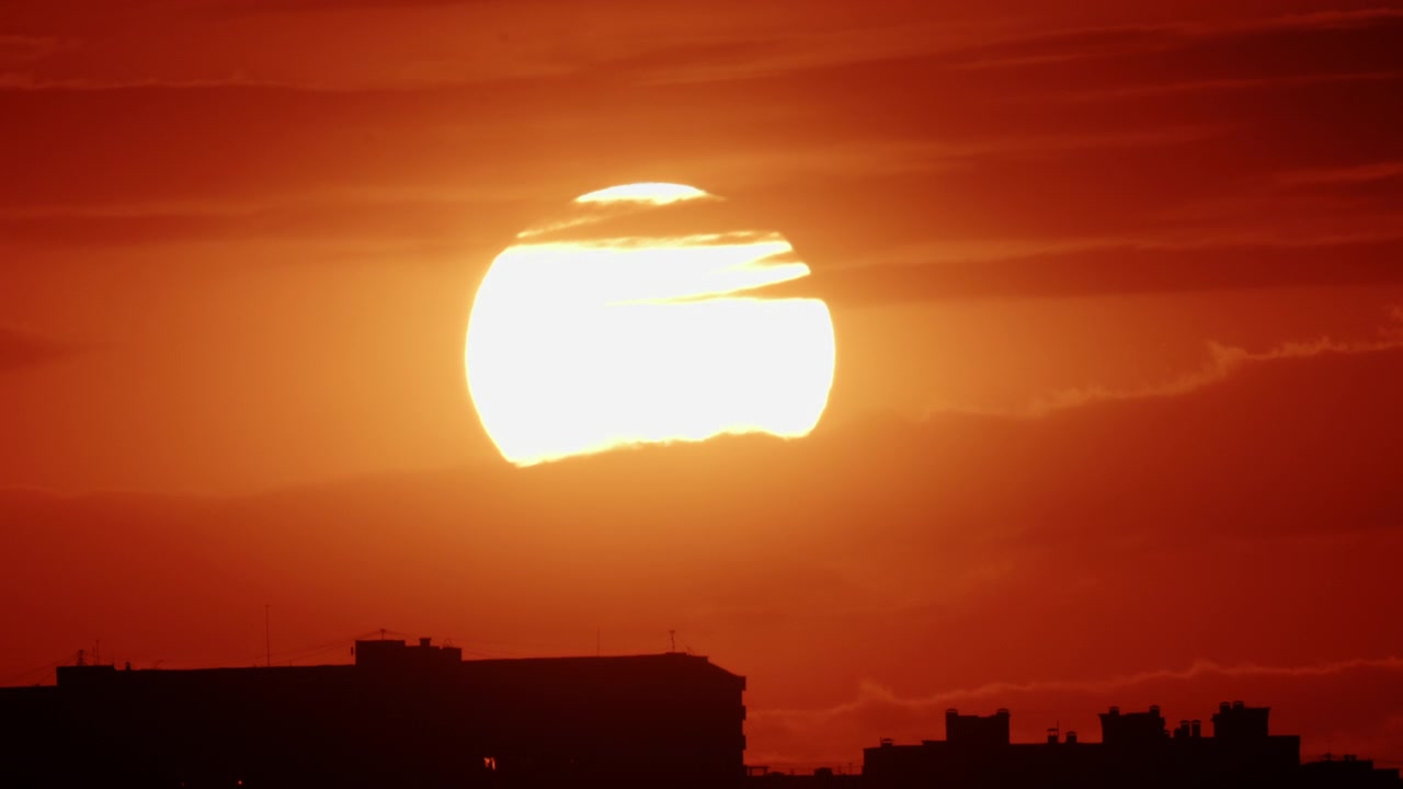 密集した都市のスカイラインの向こうに沈む黄金の夕日。中層の住宅ビルがシルエットになっている。