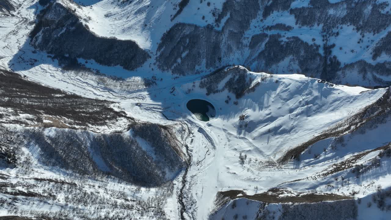 aerial shot of A deep valley surrounded by towering, snow-laden peaks, showcasing dramatic slopes and frozen river paths