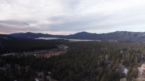 Low-panning-aerial-shot-of-an-alpine-forest-with-Big-Bear-Lake-in-the-distance-during-winter-in-California