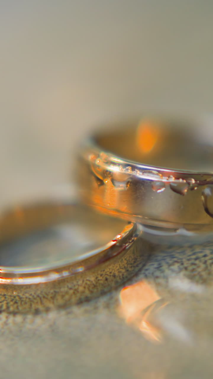 Elegant pair of shiny gold wedding rings lies in clear running water flow and bokeh effect closeup slow motion. Festive accessories