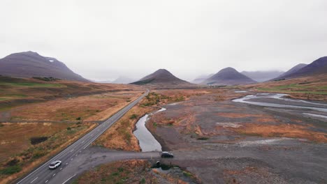 Aéreo:-Revela-Y-Sigue-Un-Todoterreno-Blanco-Que-Viaja-A-Lo-Largo-De-La-Carretera-De-Circunvalación-De-Islandia,-Que-Es-Una-Carretera-Panorámica-Que-Atraviesa-Una-Pintoresca-Y-Remota-Zona-De-Fiordos-Que-Conduce-A-Picos-Gemelos-Con-Niebla-Y-Neblina-En-La-Distancia