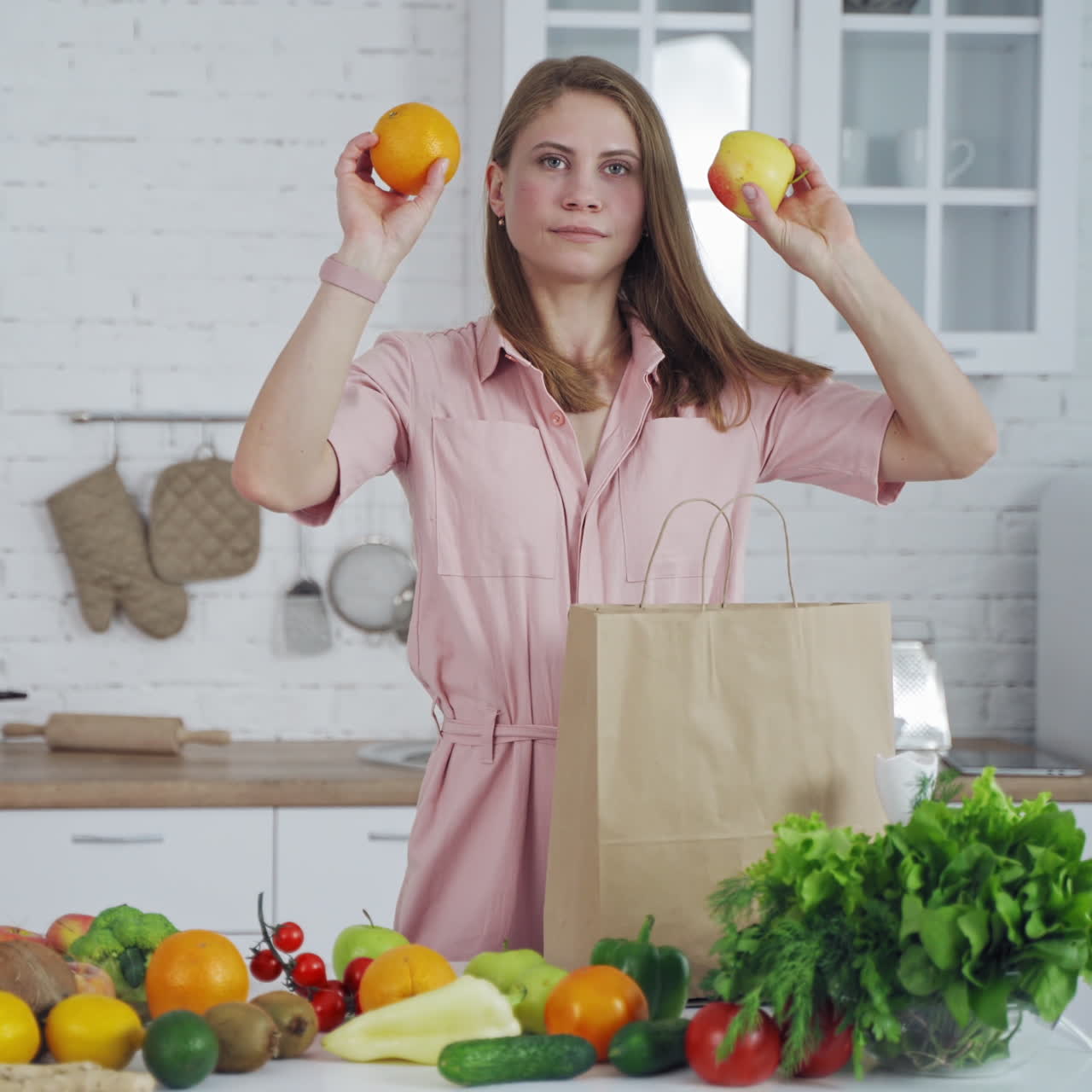 Lovely young woman takes out of a bag organic fruit in the light kitchen. Young model cares about healthy diet. Healthy food on the table.