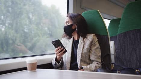 businesswoman on train using mobile phone wearing ppe face mask during health pandemic