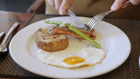 POV-to-the-dish-of-fried-egg-while-a-man-using-fork-and-knife-to-cut-it