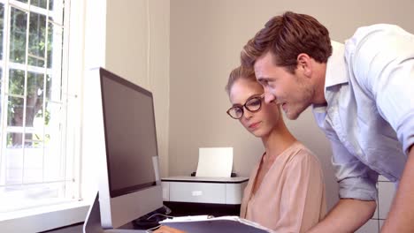 Serious-woman-working-on-computer-while-man-showing-a-file