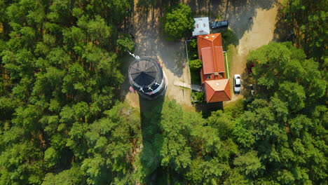 Aerial-close-up-view-of-Stilo-Lighthouse-and-green-forest-around-it---lighthouse-located-in-Osetnik-on-the-Polish-coast-of-the-Baltic-Sea,-close-to-the-village-of-Sasino,-flying-up