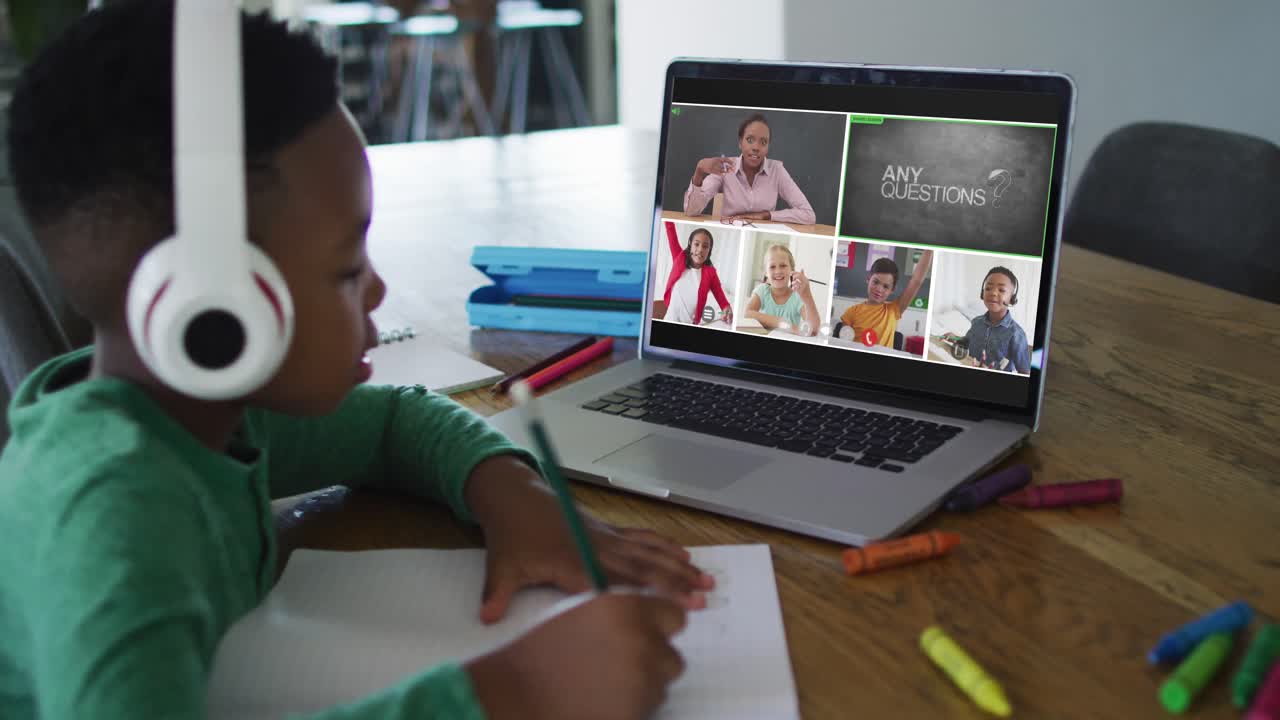 Schoolboy using laptop for online lesson at home, with diverse teacher and class on screen