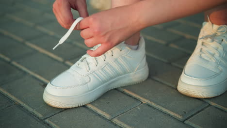 close-up of person tying shoelaces of white sneakers on interlocked pavement path, hands carefully adjusting laces for a secure fit, detailed shot emphasizes hand movement