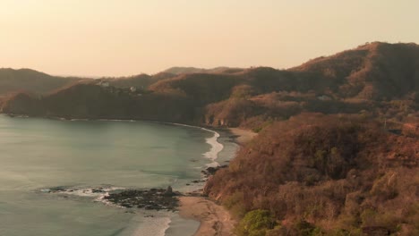 Aerial-sunset-flight-above-Flamingo-Beach-with-rock-formation-and-mountain