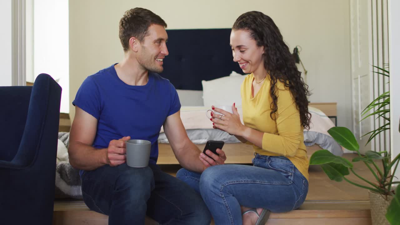 feliz pareja caucásica bebiendo café y usando un teléfono inteligente