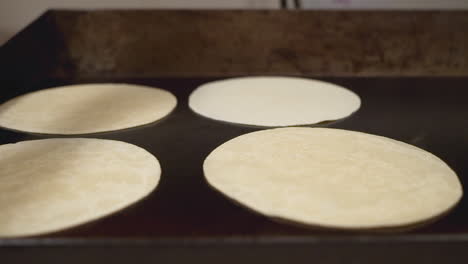 kitchen worker cooks flour tortillas on hot flat top griddle, slow motion trucking shot hd