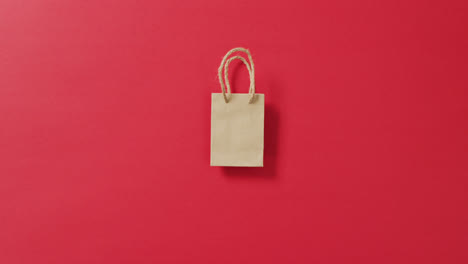 Small-brown-gift-bag-with-string-handles-on-red-background-with-copy-space