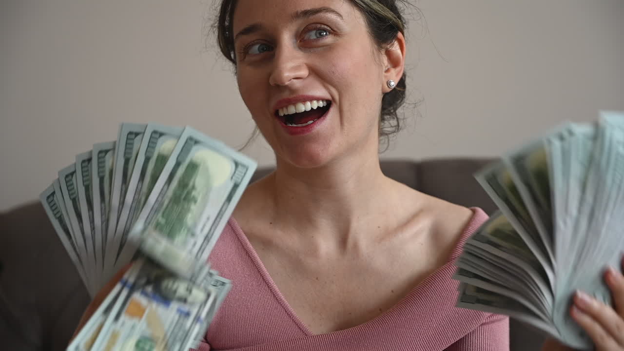 Smiling woman admiring large fans of one hundred dollar bills in her hands