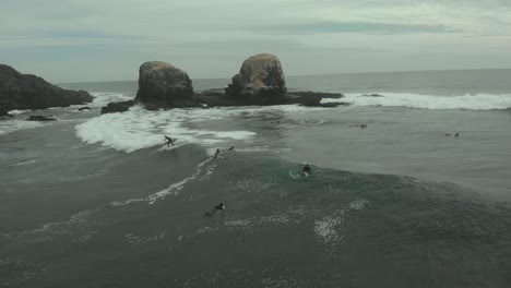 aerial of pro surfer riding wave next to giant rocks on a cold cloudy day, pichilemu, chile-4k