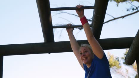 determined woman exercising on monkey bar during obstacle course