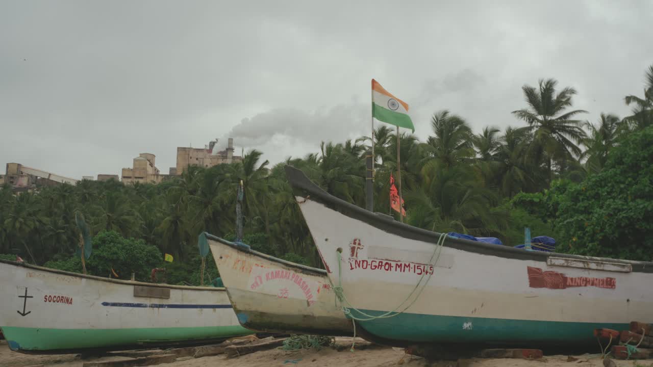 Traditional Indian fishing boats rest on a quiet beach under overcast skies, with an Indian flag flying proudly among palm trees