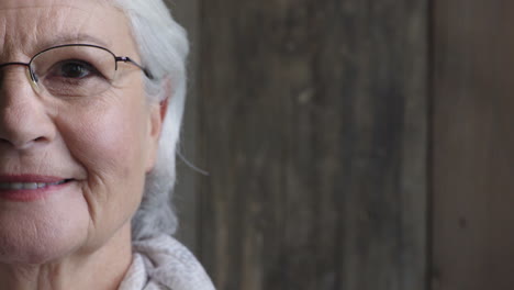 half face portrait of happy elderly woman smiling looking at camera cheerful wearing glasses on wooden background