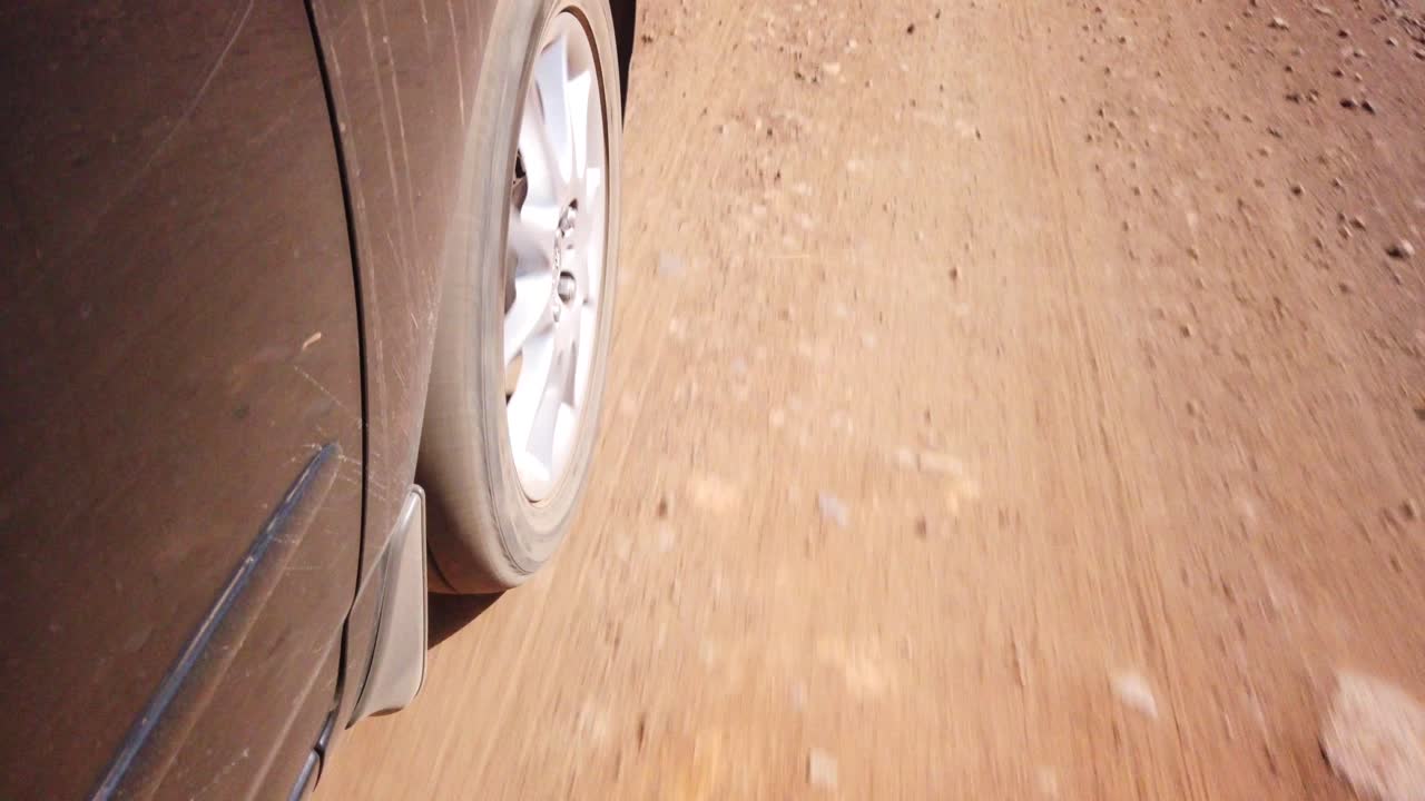 Close up of a car wheel driving on a sand gravel road