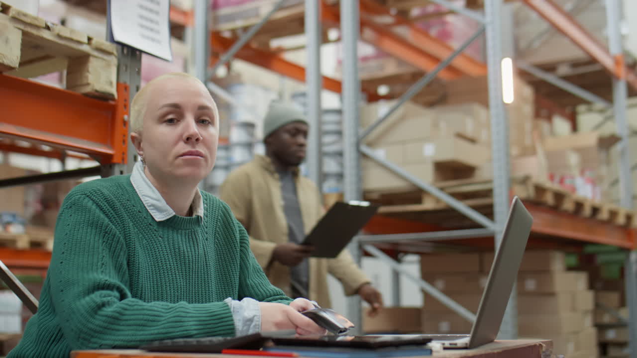 Woman Working on Laptop and Phone in a Warehouse