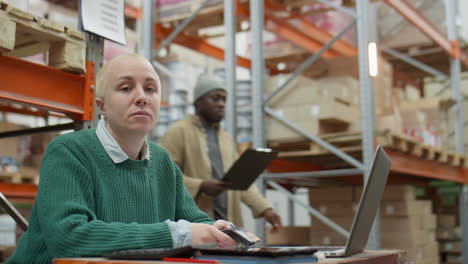 woman working on laptop and phone in a warehouse