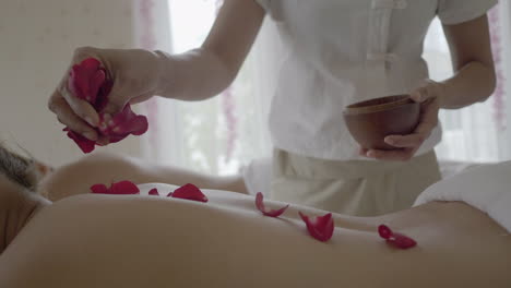 professional rose petals aromatic spa massage, therapist is putting flower parts on the back of the laying person on the massage table, well being and health concept